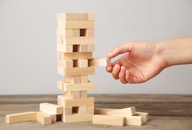 Business woman hand pick and put last piece block of the wood puzzle. Wooden block on grey wall