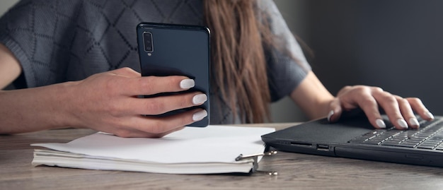 Business woman hand uses a mobile phone and works in a laptop computer