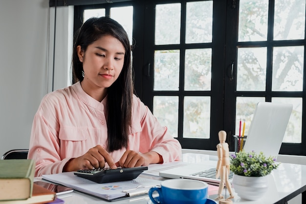 Business woman hand working with financial data and calculator on white desk in modern off