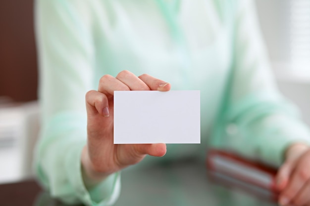 Business woman hands in a green blouse sitting at a desk in an office and holds out business card.