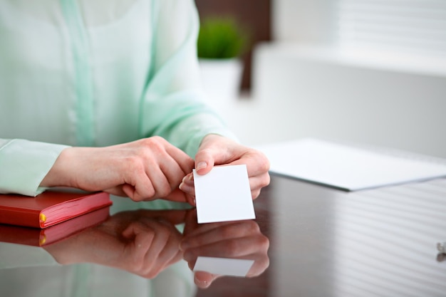 Business woman hands in a green blouse sitting at a desk in an office and holds out business card.