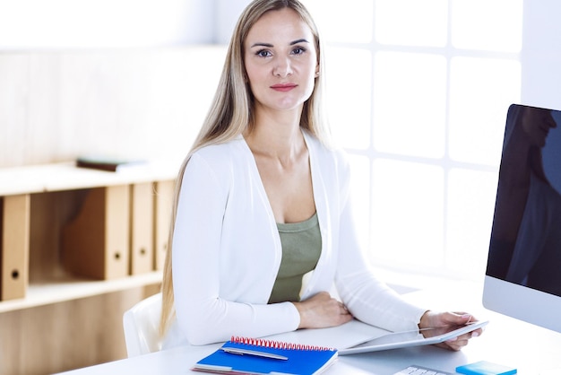 Business woman headshot while working with computer at the desk in modern office. Designer or female lawyer looks beautiful in white casual clothes. Business people concept.