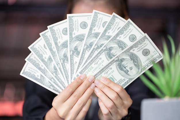 Business woman in her office holding Dollar bill fan