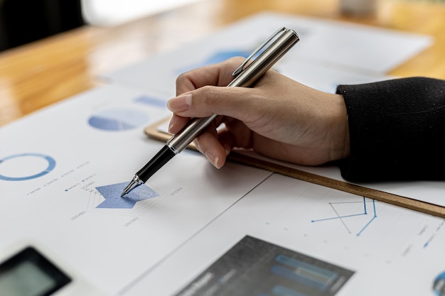 Business Woman holding a pen pointing to a bar graph document of company financial data, she is reviewing the company's monthly financial documents. Finance concepts and money management.