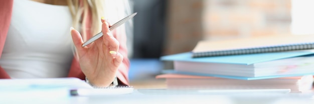 Business woman holding silver ballpoint pen at table with folders closeup