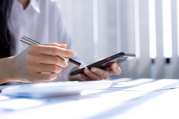 Business woman holding a smartphone and pointing at the screen, she is typing a chat message with her partner using a smartphone messenger. Concept of using technology in communication.