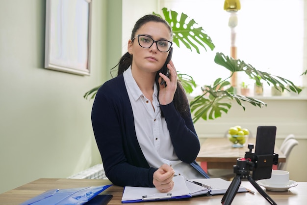 Business woman looking into smartphone webcam talking online recording video