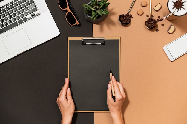 Business woman make paperwork, hold clipboard and pen over trendy workspace coffee design top view. Blank paper layout, laptop, stationery on table.