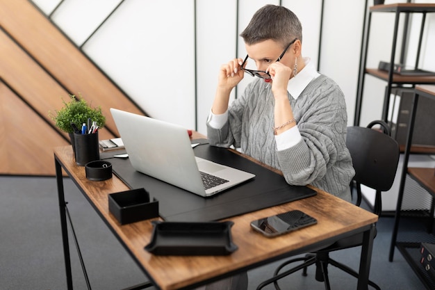 Business woman in the office sitting in front of a laptop looking at the screen through glasses