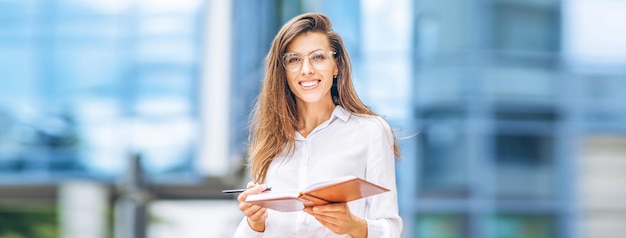 Business woman outdoors near modern business center with notebook