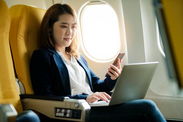 Business woman In a plane works on using laptop computer and phone