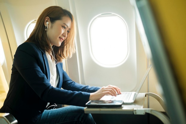 Business woman In a plane works on using laptop computer and phone