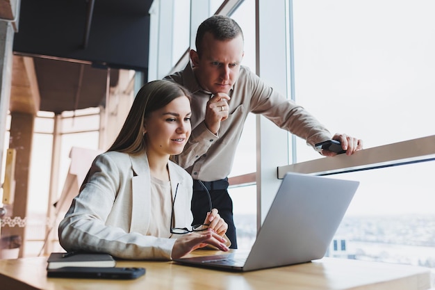 Business woman pointing her finger at a laptop for a male colleague Business cooperation and teamwork European millennials at the table in the office Modern successful people