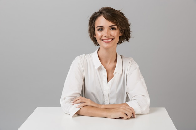 Business woman posing isolated over grey wall sitting at the table