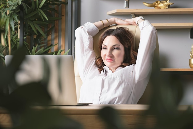 Business woman sits at her desk and put her hands behind her head