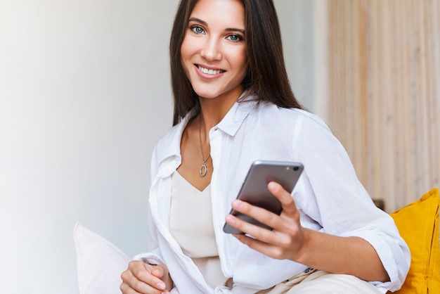 Business woman sits at table in front of laptop, writes a message using smartphone, conducts business correspondence at work. Beautiful brunette girl uses gadgets for work. Online remote work.