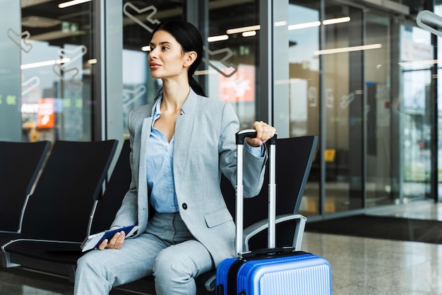 Business woman sitting in airport and waiting for starting her travel voyage Woman with luggage is holding handle of the suitcase and looking around airport terminal