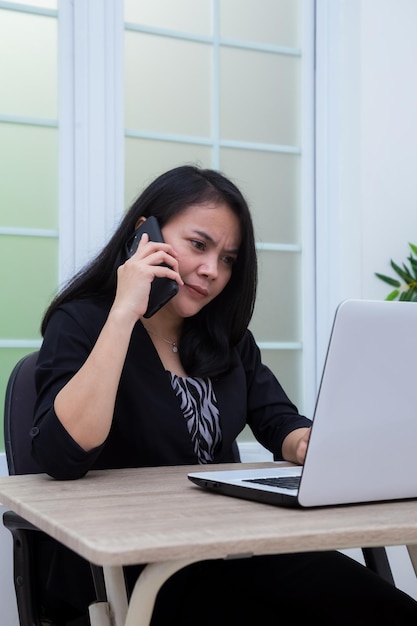 Business woman sitting on chair making phone call in front of laptop with confused facial expression