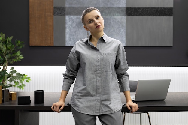 A business woman stands leaning on a table against the backdrop of a modern stylish office