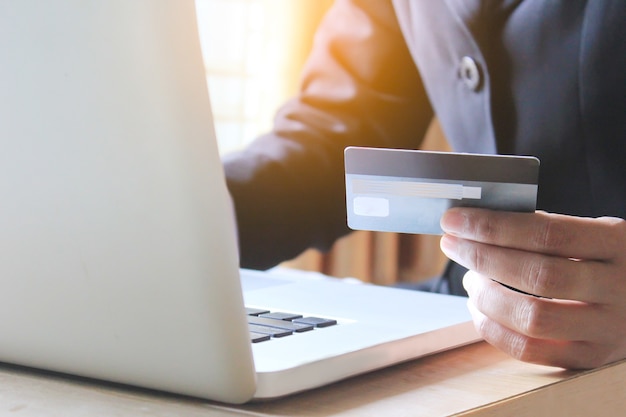 Business woman in suit hands holding credit card and using laptop