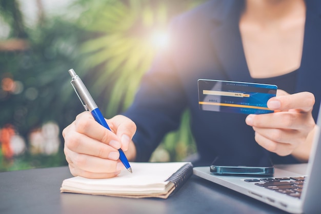 Business woman taking notes with pen on notebook and use a credit card to shop online.