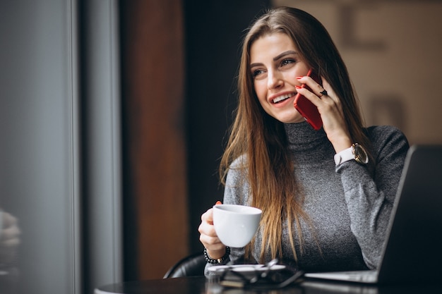 Business woman talking on a phone and drinking coffee in a cafe