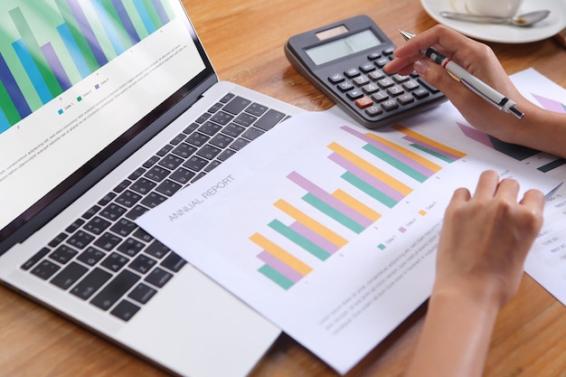 Business woman using calculator calculate annual report with laptop and office stationery on wooden desk