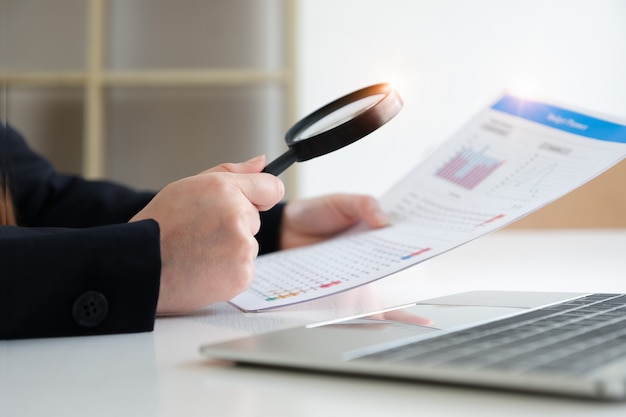 Business woman using magnifying to review balance sheet annual. Audit and Check integrity before investment concept.