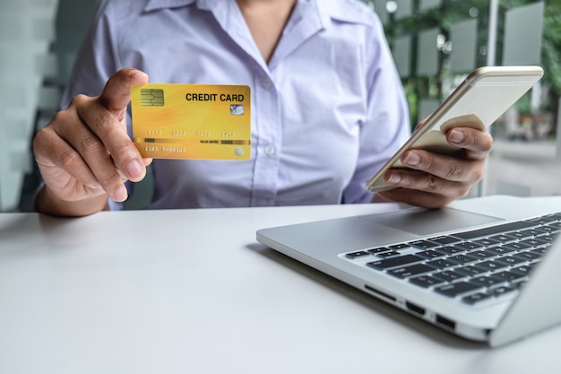 Business woman using smartphone, laptop and holding credit card for paying detail page display online shopping purchase and entry security code to inputting card information.