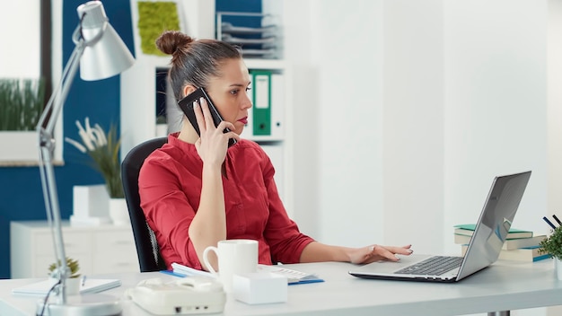 Business woman using smartphone to talk to project manager, working on charts statistics. Company employee having phone call conversation in startup office to do financial research.