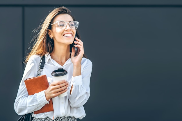 Business woman walking and talking on the cellphone outdoors near modern business center with notebook.