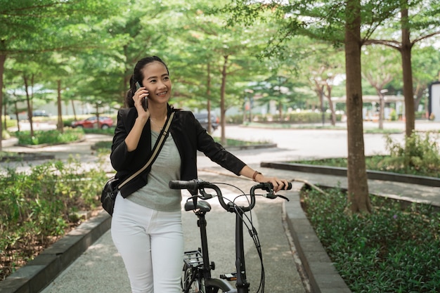 Business woman walks with her folding bike while receiving a telephone call