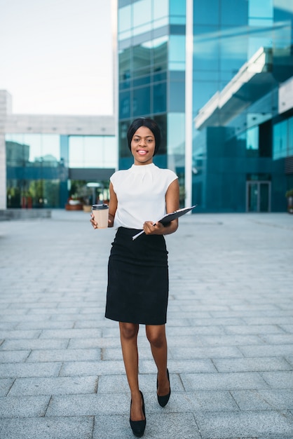 Business woman with cardboard coffee cup and notepad outdoors