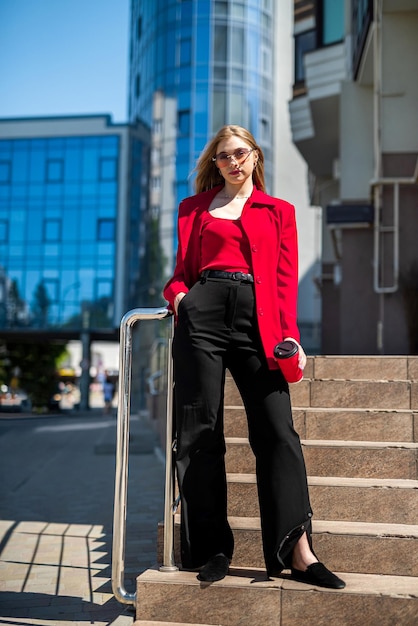 A business woman with a cup of coffee is talking on her smartphone while standing in the middle of the city center The concept of a woman who earns money