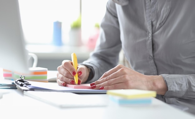 Business woman with red manicure writing with pen on paper stickers closeup