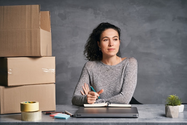 Business woman working from home with laptop and notepad preparing boxes with products for delivery