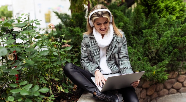 Business woman working on laptop with headphones outside