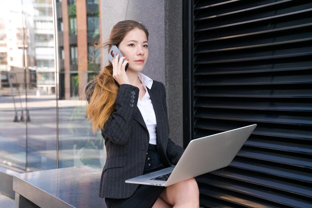 Business woman working on street Young woman is sitting on bench with laptop