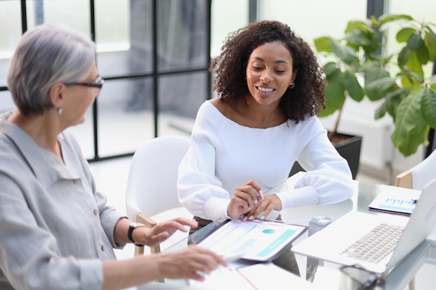 Business women smile while working together on a laptop at a table in the boardroom in the office