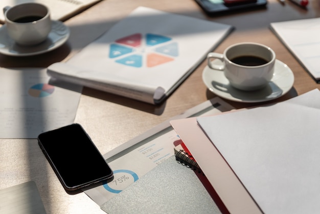 Business and work concept. Closeup of smartphone on woking desk with document, chart, notebook, and cup of hot black coffee.