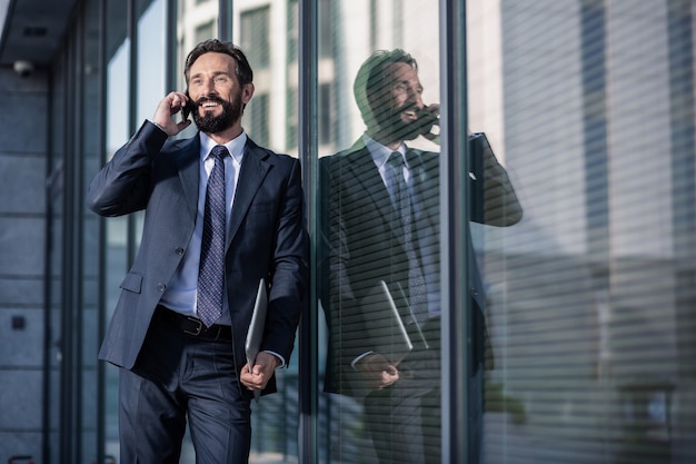 Business world. Cheerful delighted businessman talking on phone and smiling