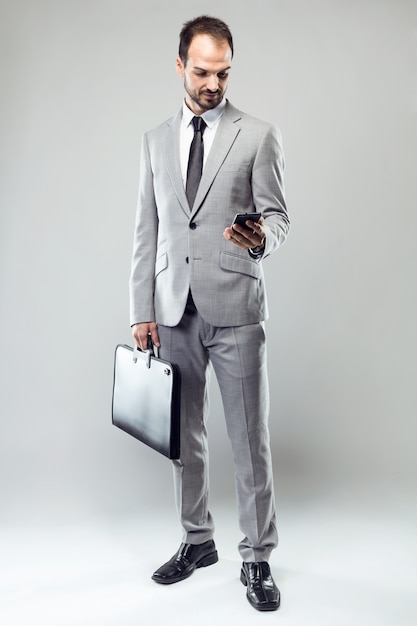 Business young man using his mobile phone over gray background.