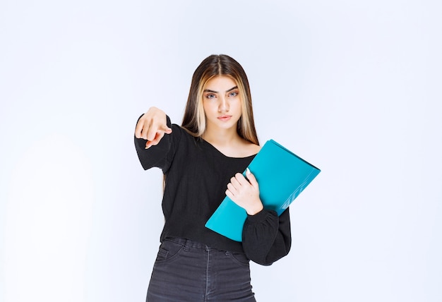 Businesslady holding a blue folder and pointing at her colleague. High quality photo