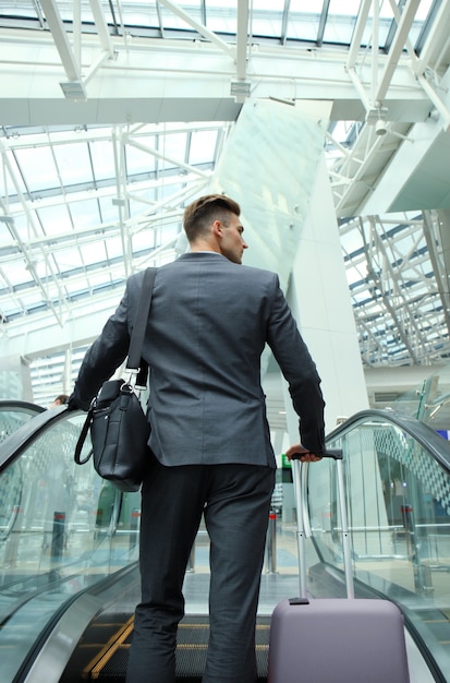 Businessman at the airport going down the escalator.