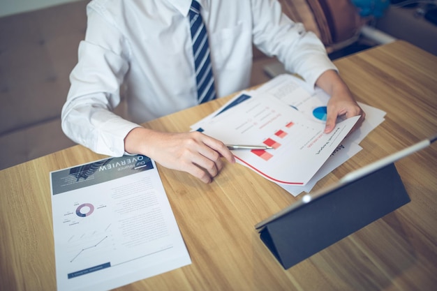 Businessman analyzing bar graph data with pen in hand laptop and coffee on desk Business concept