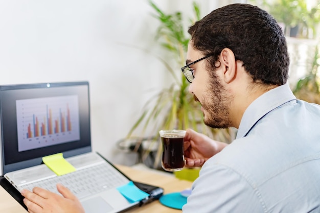 Businessman analyzing statistic on laptop while having coffee at office