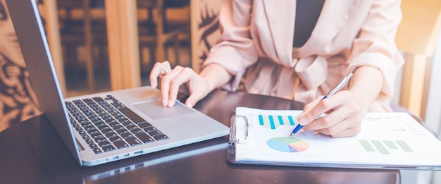 Businessman analyzing the stock situation.She uses a pen and a laptop computer.For web banner.