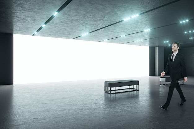 Businessman in black suit in a spacious modern hall with big blank white screen