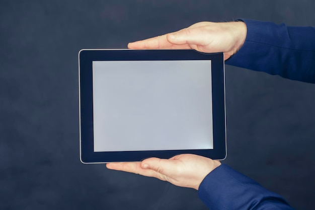 Businessman in a blue jacket holds a mockup of a tablet with a white screen on a dark background