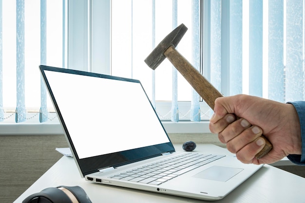 Businessman breaks a laptop with an empty white screen with a hammer empty blank laptop screen for design or text message copy space